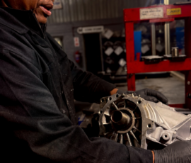 Technician holding an opened manual gearbox casing beside the workshop press